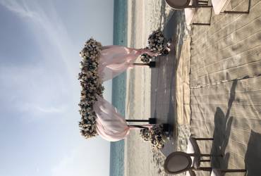 Outdoor wedding setup on white sand at Saadiyat Beach Club with a scenic views of the Aegean Sea and clear blue skies.