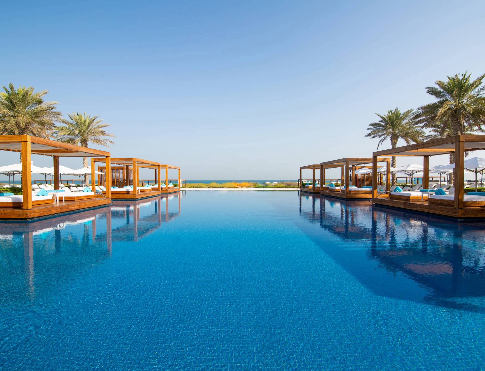 The inviting pool at Saadiyat Beach Club, lined by floating cabanas and palm trees, with the Aegean Sea in the background