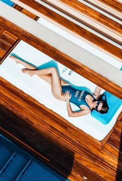 Woman in a swimsuit and sunglasses laying down by the pool enjoying the relaxed atmosphere at Saadiyat Beach Club.