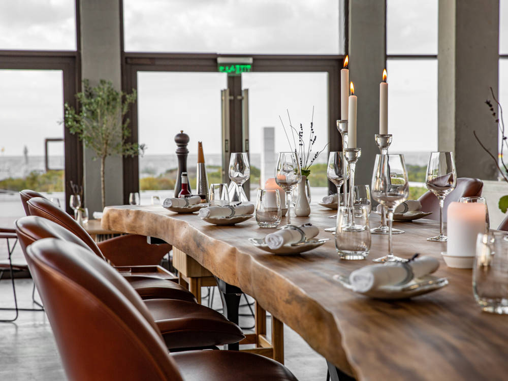 Dining area at Saadiyat Beach Club featuring a rustic solid wood table, elegantly adorned with candles and plants.
