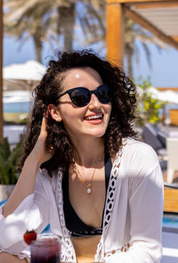 Close-up of a woman with curly hair relaxing beside a poolside cabana at Saadiyat Beach Club in Abu Dhabi.